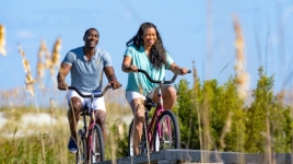 A man and woman bike along a boardwalk.